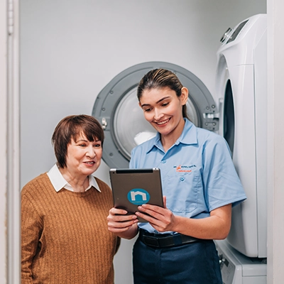 Mr. Appliance service professional viewing a tablet with a customer next to her washing machine.