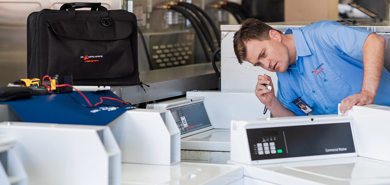 Mr. Appliance service professional inspecting the back of a commercial washing machine.